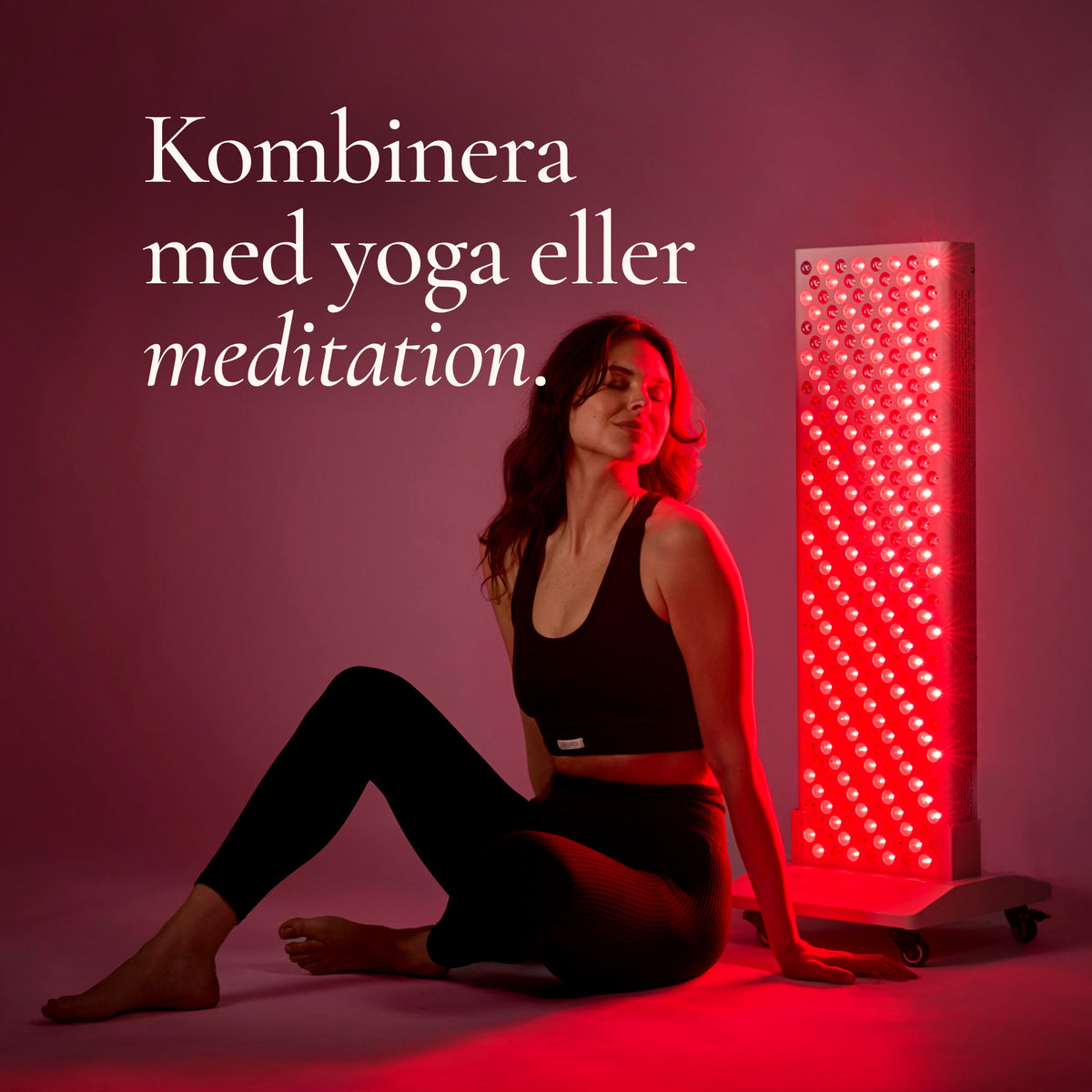 Kvinna sitter avslappnad på golvet framför den tända rödljuspanelen The Red Deer. Den kan användas samtidigt som yoga eller meditation.